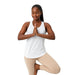 Femme en débardeur blanc en posture de yoga, équilibre sur une jambe, tenue confortable et respirante