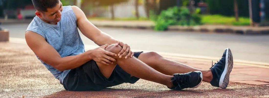 Coureur assis au sol tenant son genou douloureux, illustration des blessures en course à pied et de l’importance de la prévention et du renforcement.