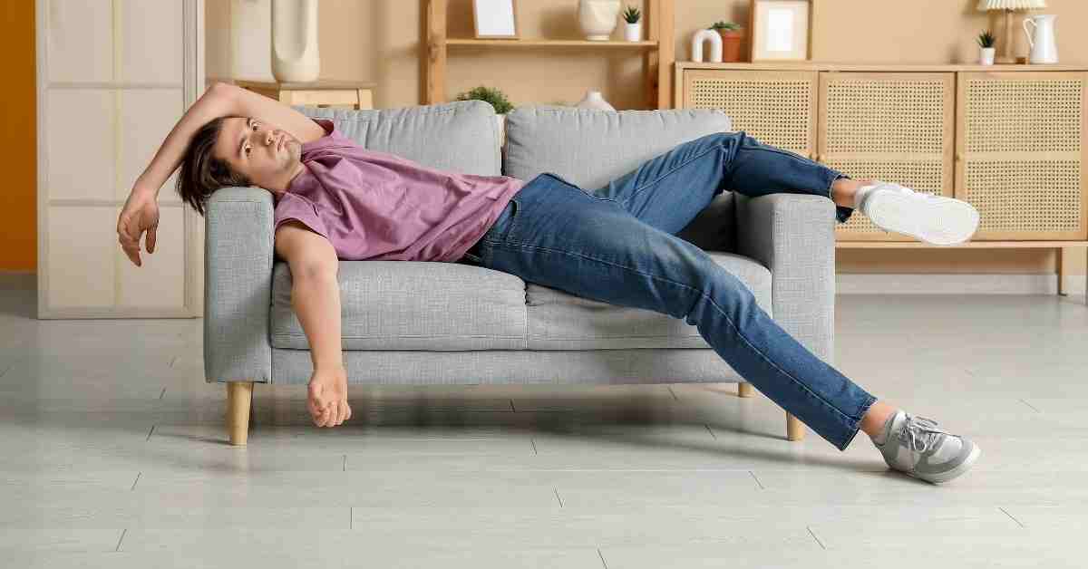 Personne allongée sur un canapé, visiblement épuisée après une journée ou une activité physique.