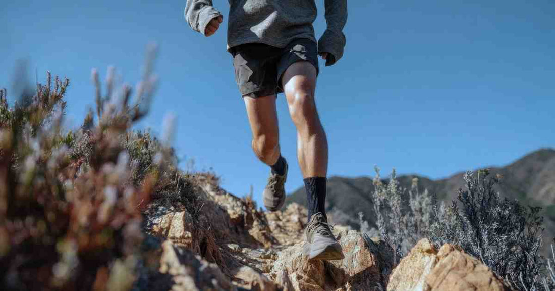 Coureur de trail en descente sur un sentier rocheux en montagne, illustrant l’effort et la technicité du terrain.