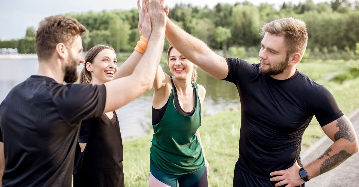 Groupe de femmes et d’hommes pratiquant une activité sportive en plein air, échangeant un geste de motivation après l’entraînement, illustrant les bienfaits du sport sur la santé mentale.