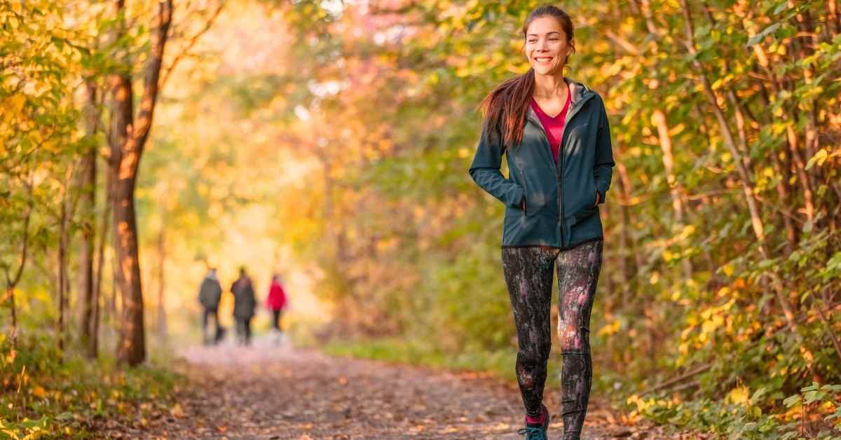Femme en tenue de sport marchant en forêt à l’automne, récupération active après un 10 km
