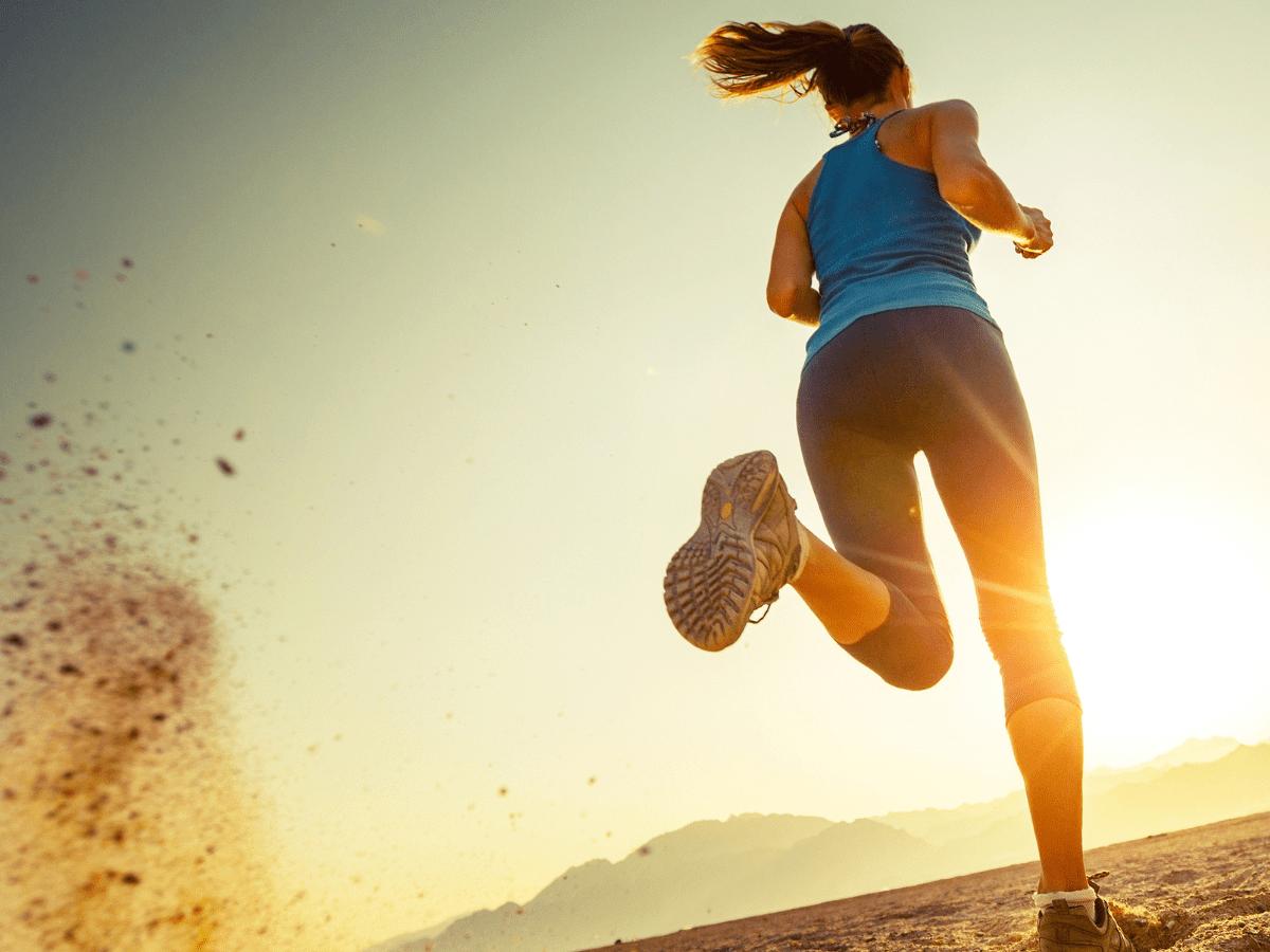 Femme en plein running sur terrain sableux – performance, énergie et tenue de sport.