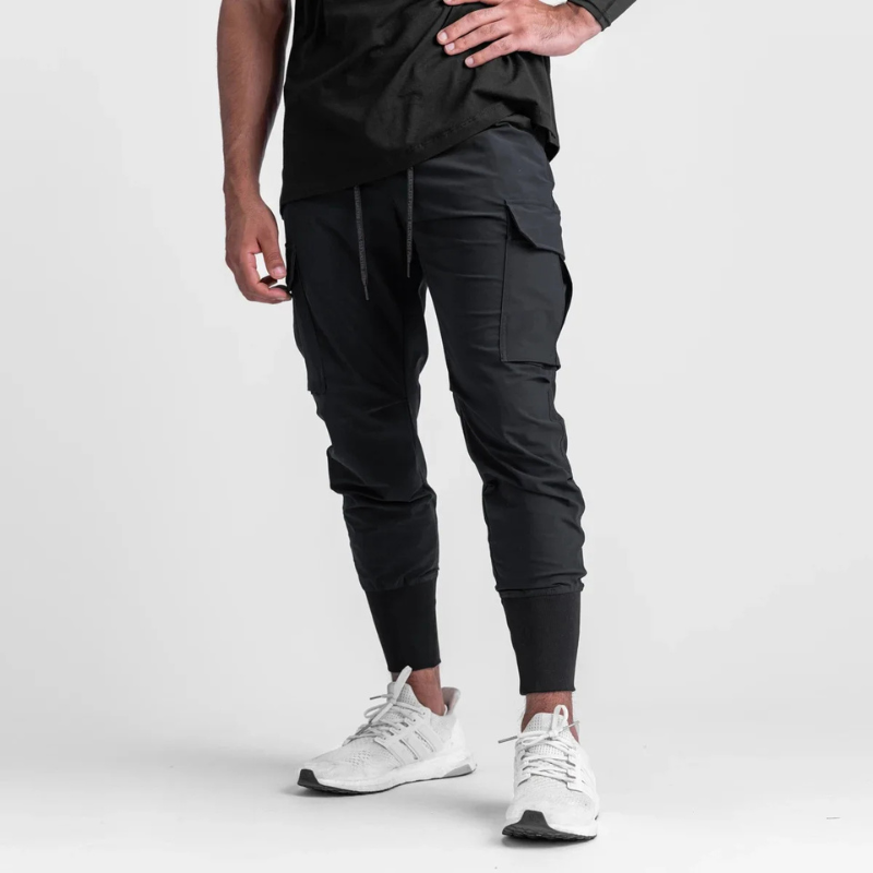 Pantalon running homme Noir Performance conçu en tissu technique stretch nylon & spandex. Sa coupe tapered avec bas élastiqué assure maintien et mobilité maximale. Parfait pour fitness, musculation et training urbain.
