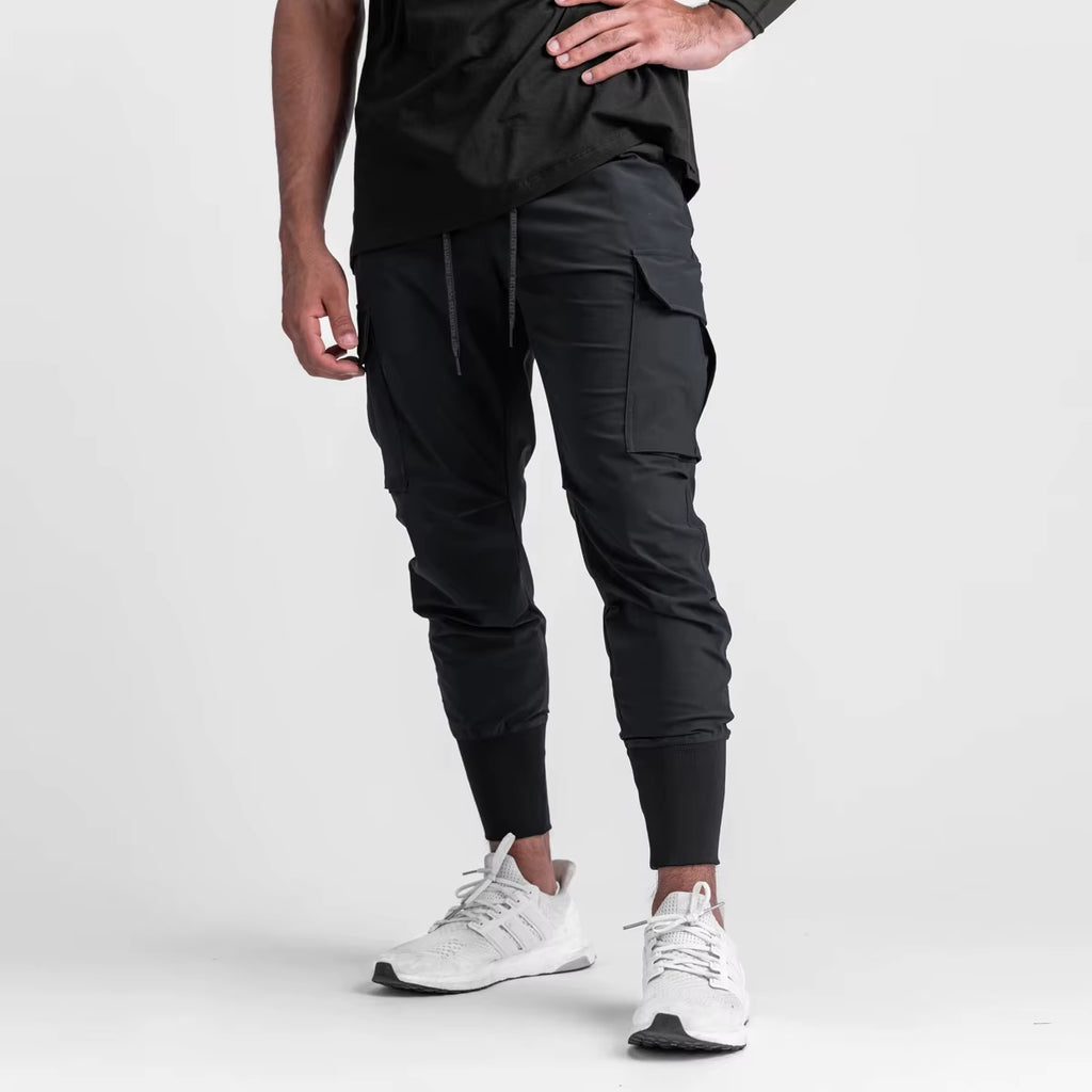 Pantalon running homme Noir Performance, conçu en nylon & spandex stretch pour accompagner chaque mouvement. Sa coupe tapered avec poches cargo et finition bas élastiqué offre stabilité, confort et style minimaliste en training urbain.
