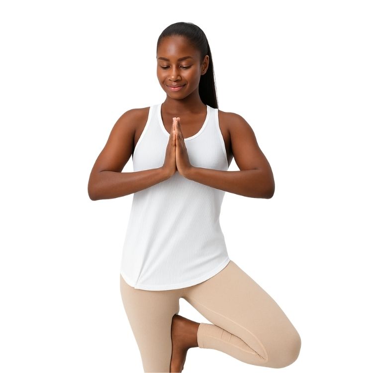 Femme en débardeur blanc en posture de yoga, équilibre sur une jambe, tenue confortable et respirante