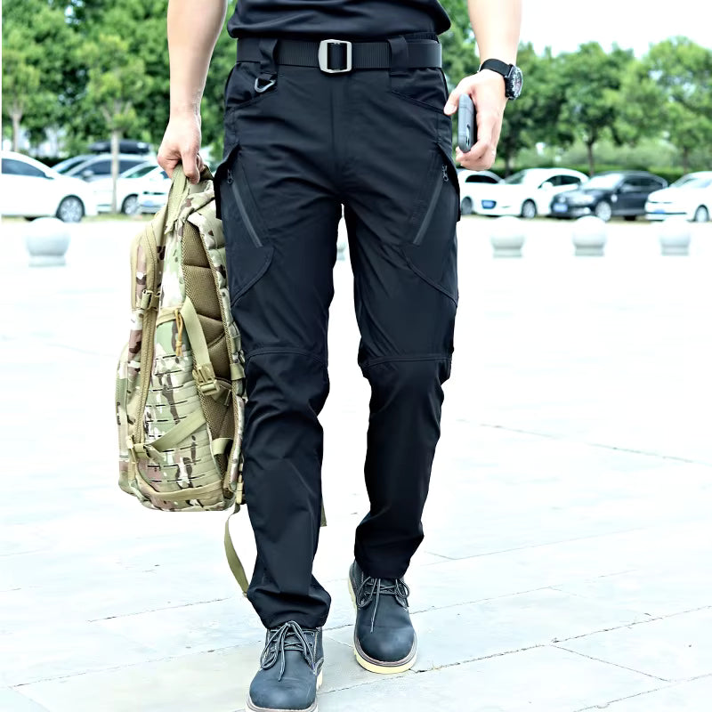 Pantalon cargo tactique homme noir porté en extérieur avec sac militaire, idéal pour randonnée, outdoor et activités terrain